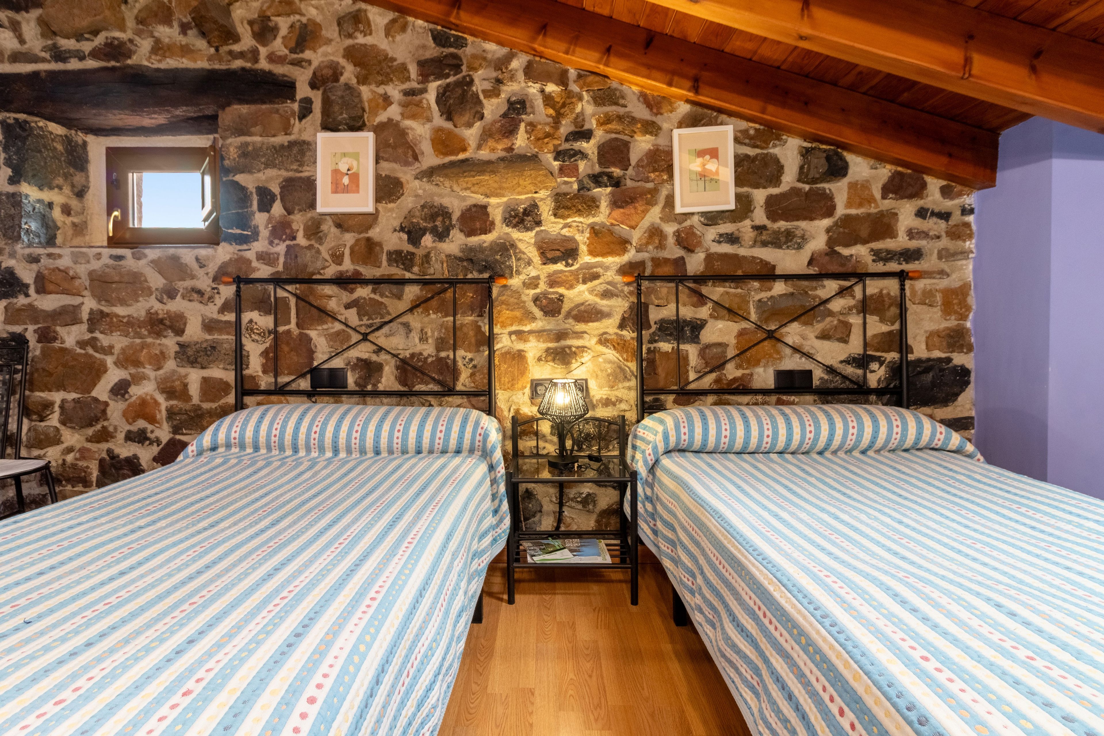 Une chambre avec deux lits, un mur en pierre et un plafond en bois.