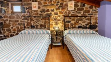 Une chambre avec deux lits, un mur en pierre et un plafond en bois.