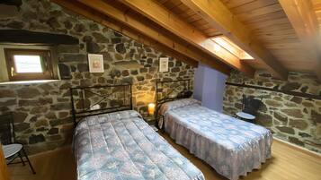 Une chambre avec deux lits, des murs en pierre, des poutres en bois, une petite table et une fenêtre.