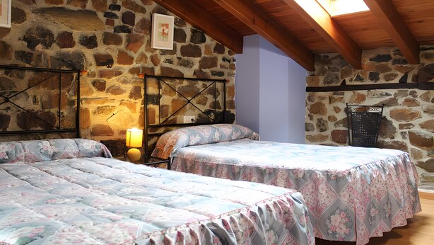 Una habitación con dos camas, una pared de piedra, techo de madera y un tragaluz.
