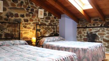 Une chambre avec deux lits, un mur en pierre, un plafond en bois et une lucarne.