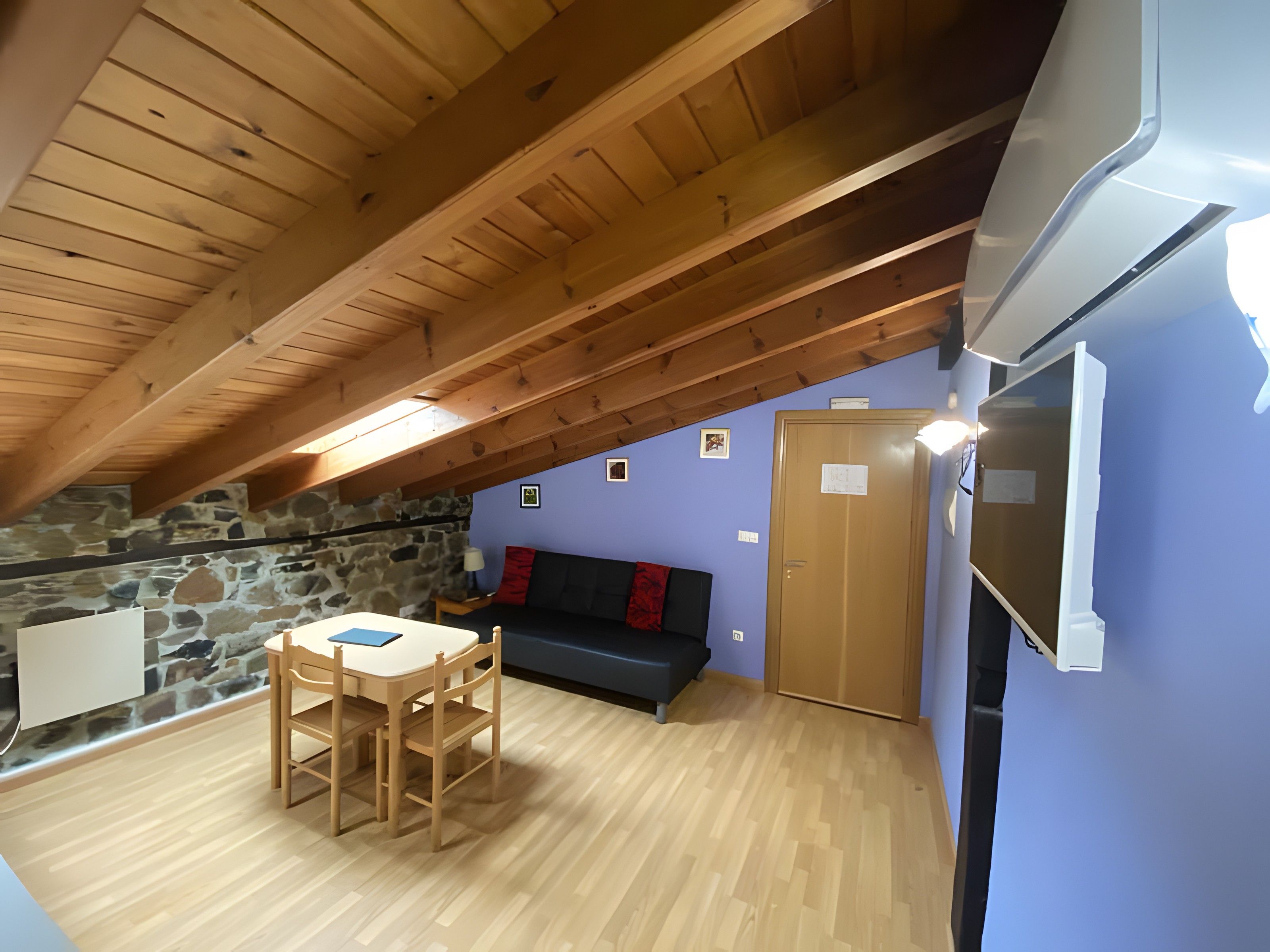 Una habitación acogedora con techo de madera, pared de piedra, pared azul, puerta de madera y refrigerador blanco.
