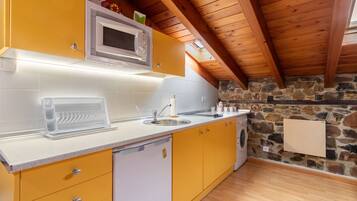 Una cocina con armarios amarillos, encimera blanca, microondas integrado, lavavajillas y pared de piedra.