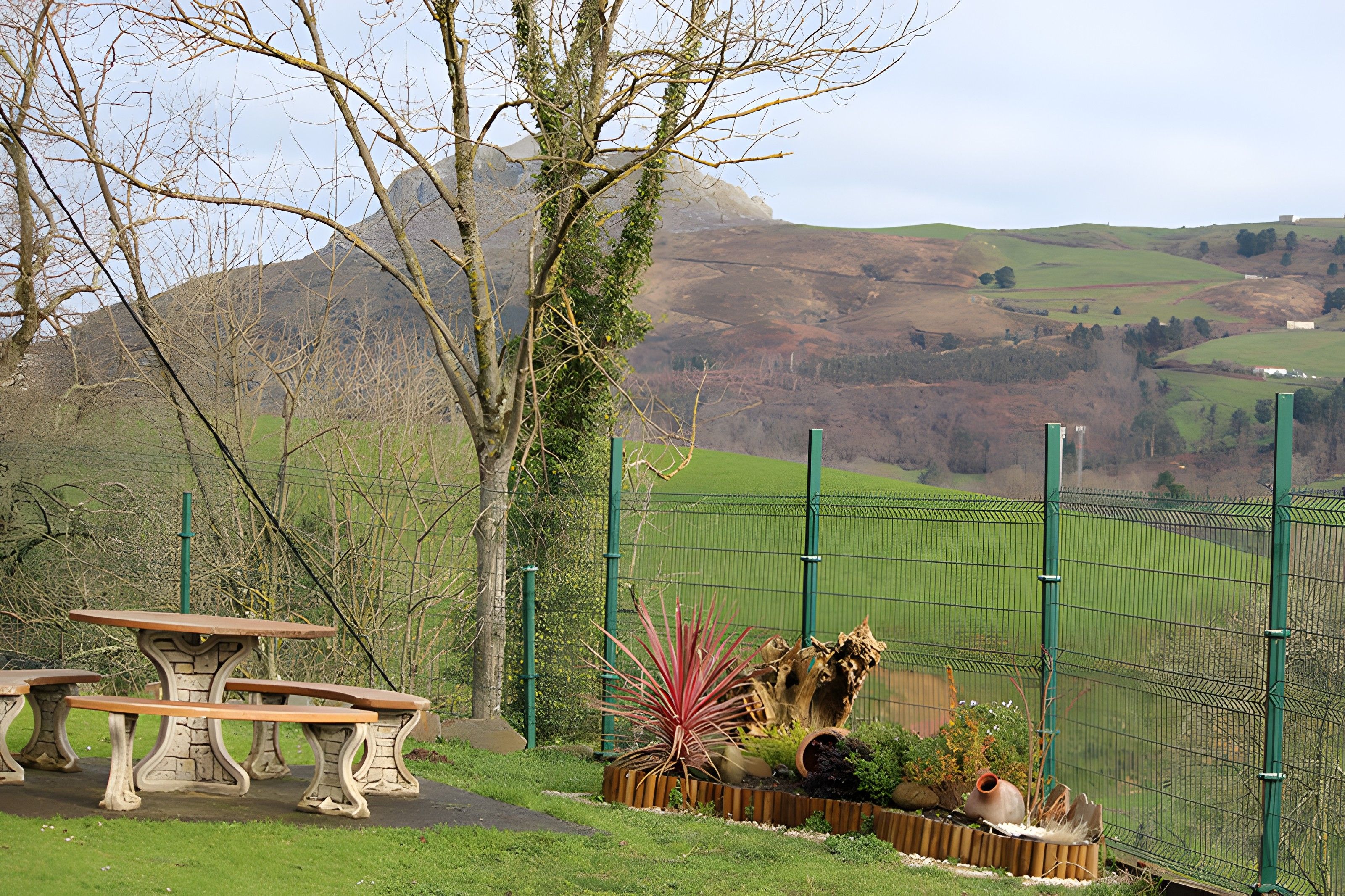A park with a stone bench, a fence, and a view of rolling hills.