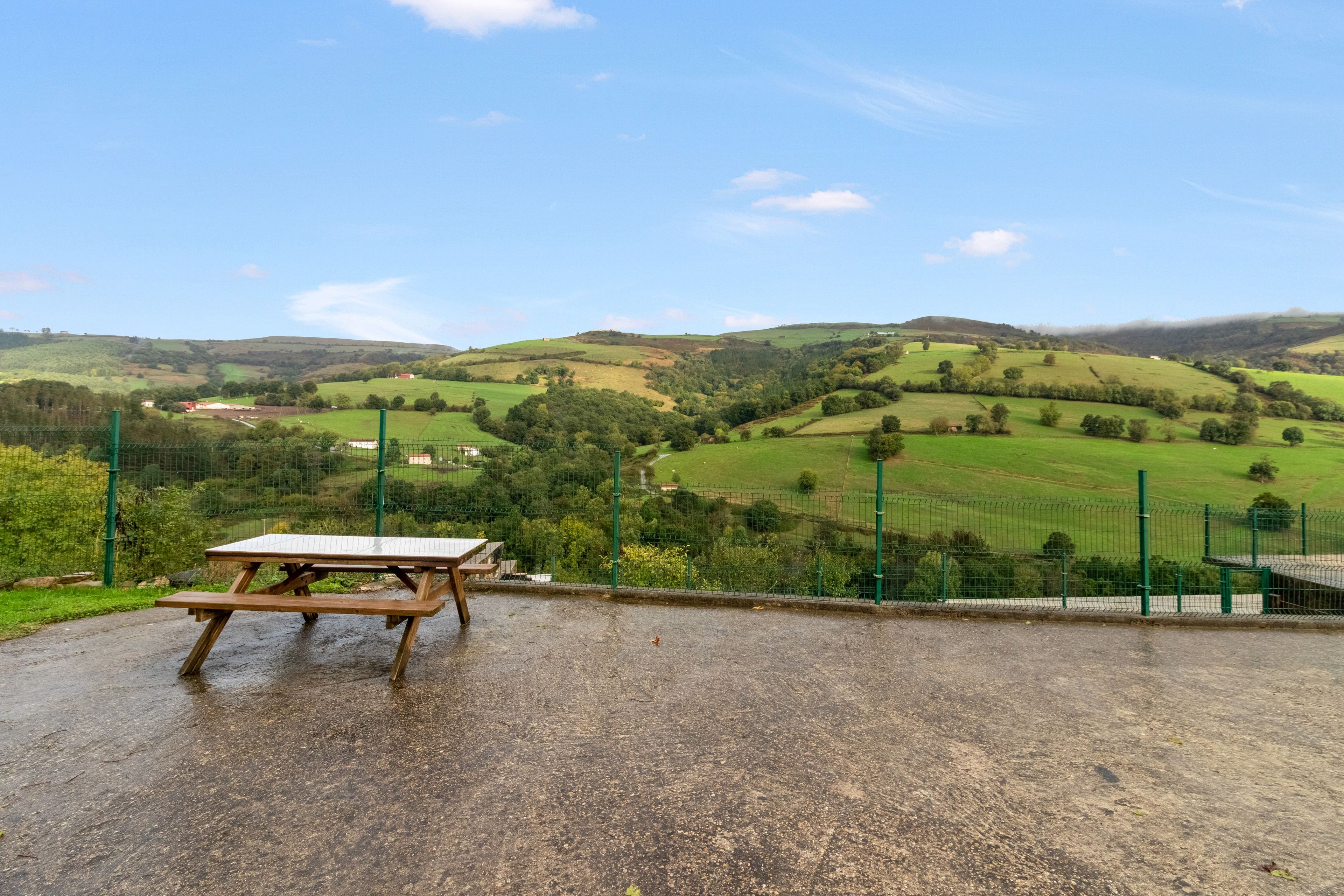 Una mesa de picnic en un entorno rural, con vistas a colinas onduladas y un cielo despejado.