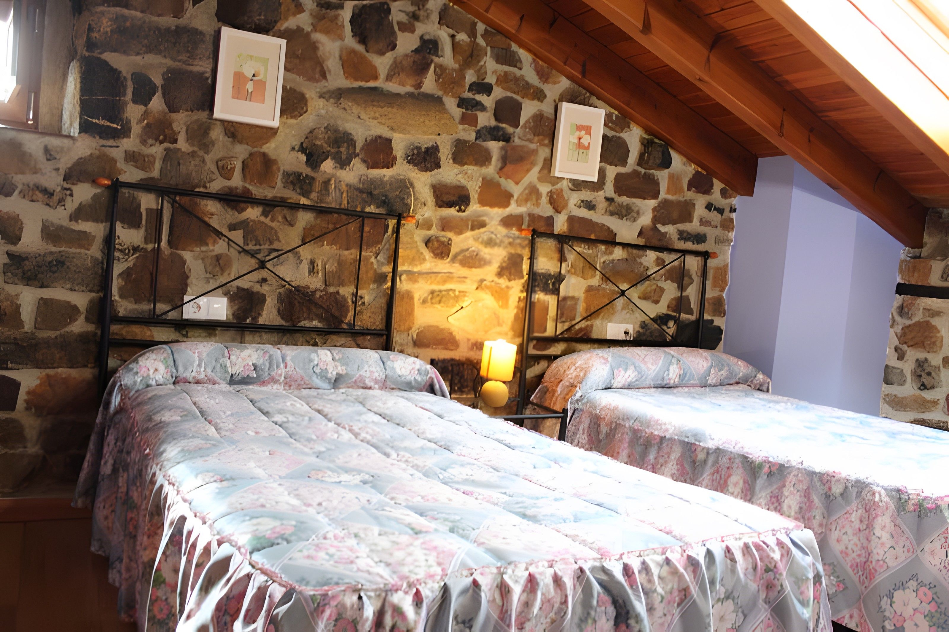 Una habitación con dos camas, una pared de piedra y techo de madera.