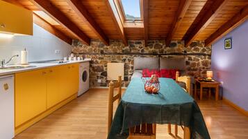 Una cocina acogedora con pared de piedra, vigas de madera, lavadora y comedor con mesa para dos.