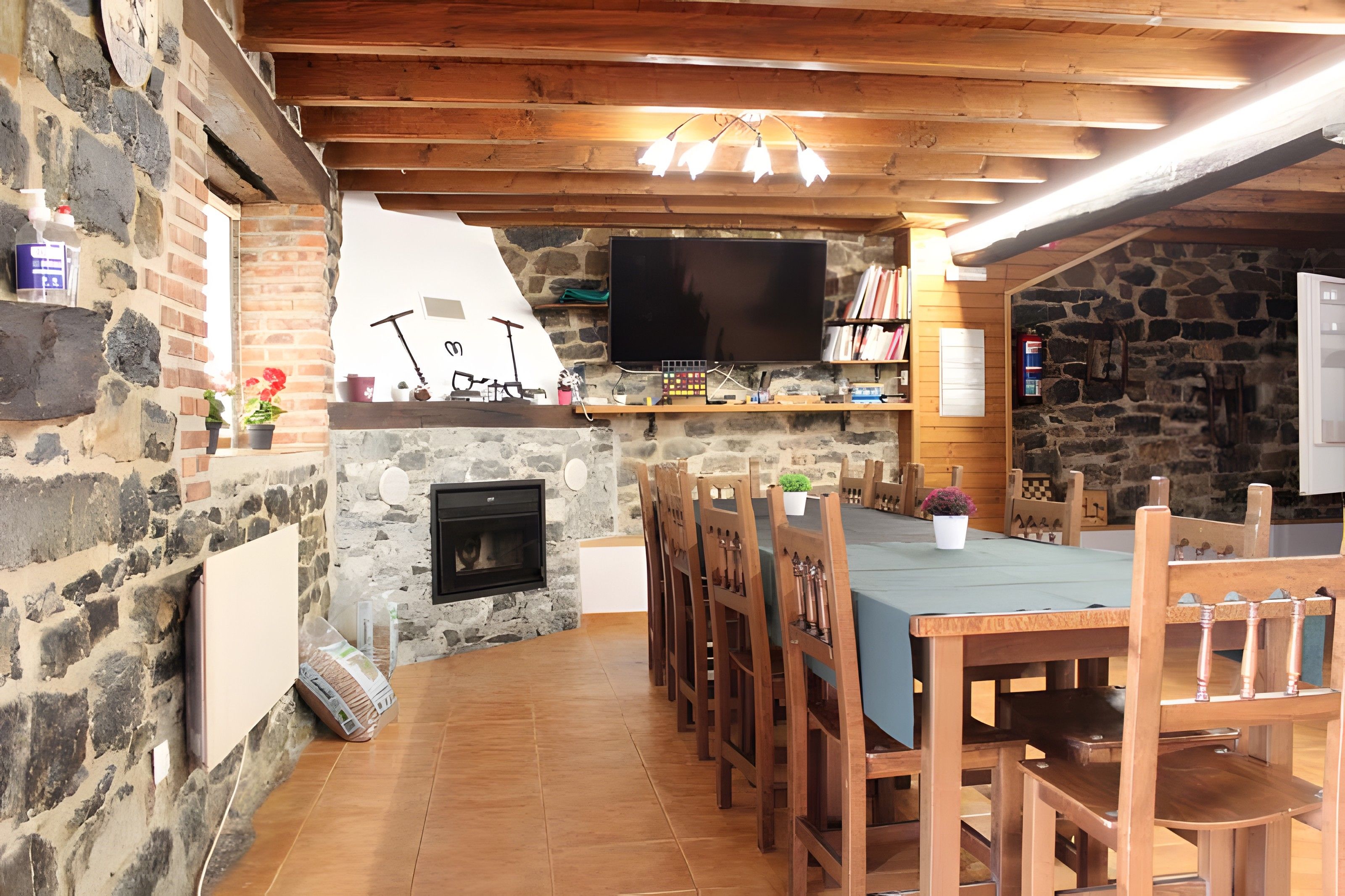 Un intérieur rustique avec un mur en pierre, un plafond en bois, une cheminée, un téléviseur et un coin repas comprenant des chaises et une table en bois.