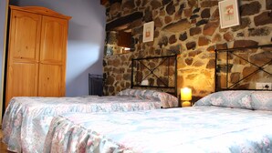 Un dormitorio con dos camas, un armario de madera y una pared de piedra.