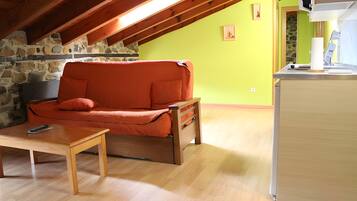 Una habitación acogedora con techo de madera, pared de piedra, un sofá, una mesita y una zona de cocina.