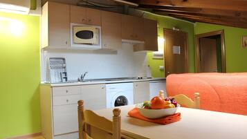 Cocina compacta con microondas, lavabo y lavadora. En primer plano, una mesa con un cuenco de fruta.