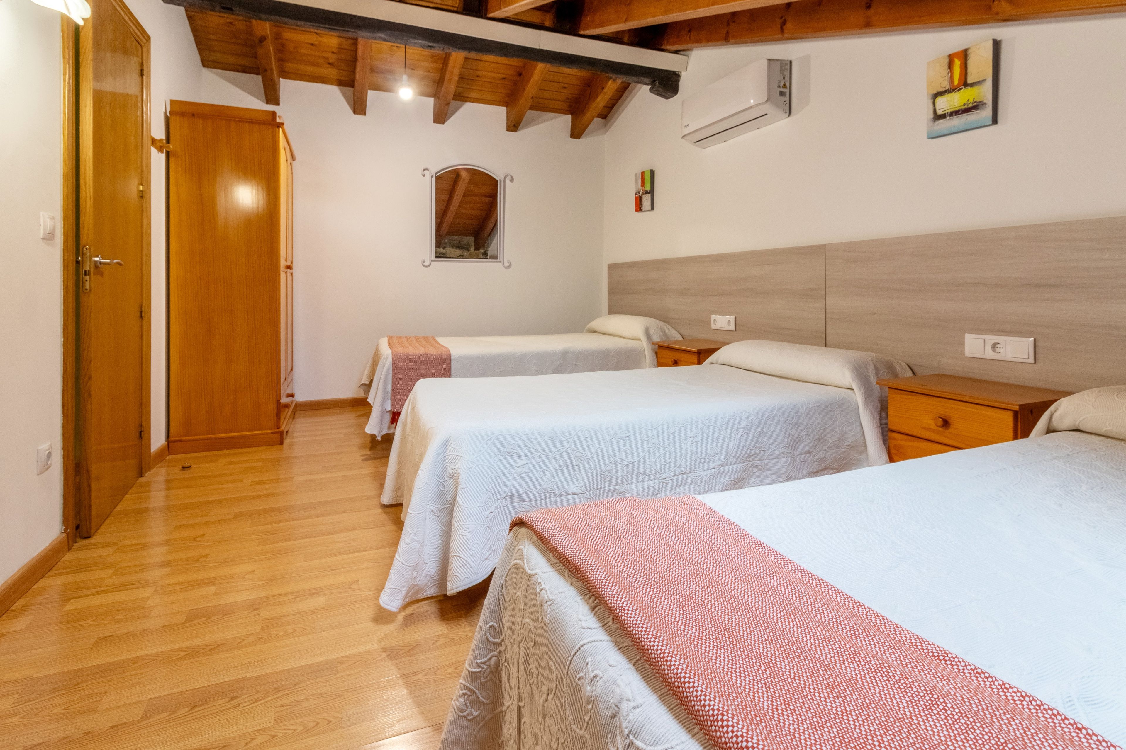 Habitación de hotel con dos camas, suelo y techo de madera, un ventanal pequeño y un aire acondicionado instalado en la pared.