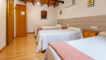 Habitación de hotel con dos camas, suelo y techo de madera, un ventanal pequeño y un aire acondicionado instalado en la pared.