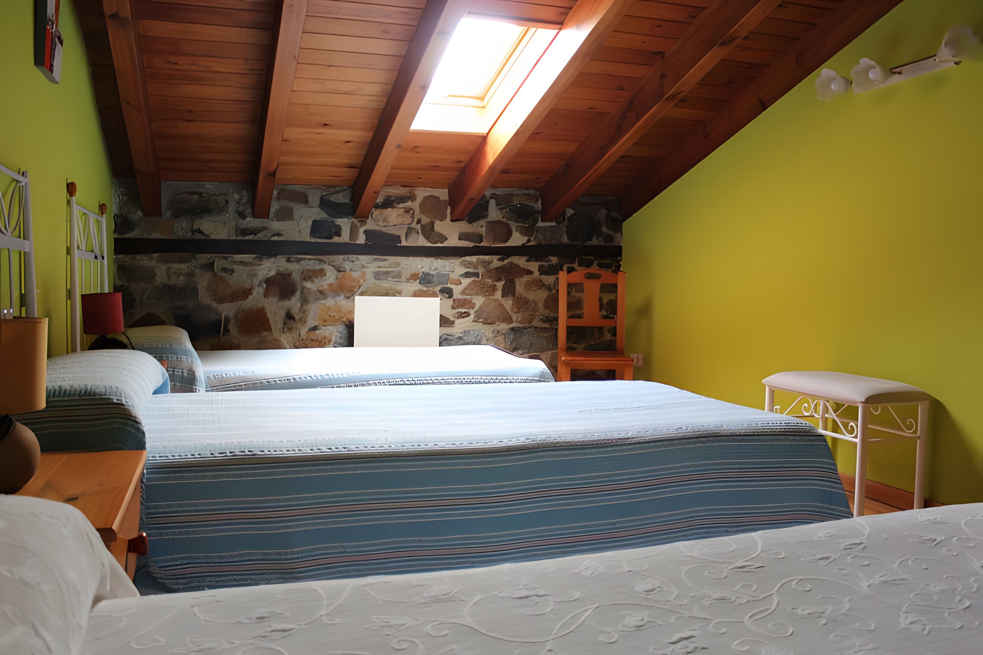 Un dormitorio con dos camas, pared de piedra, techo de madera y tragaluz.