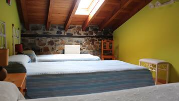 Un dormitorio con dos camas, pared de piedra, techo de madera y tragaluz.
