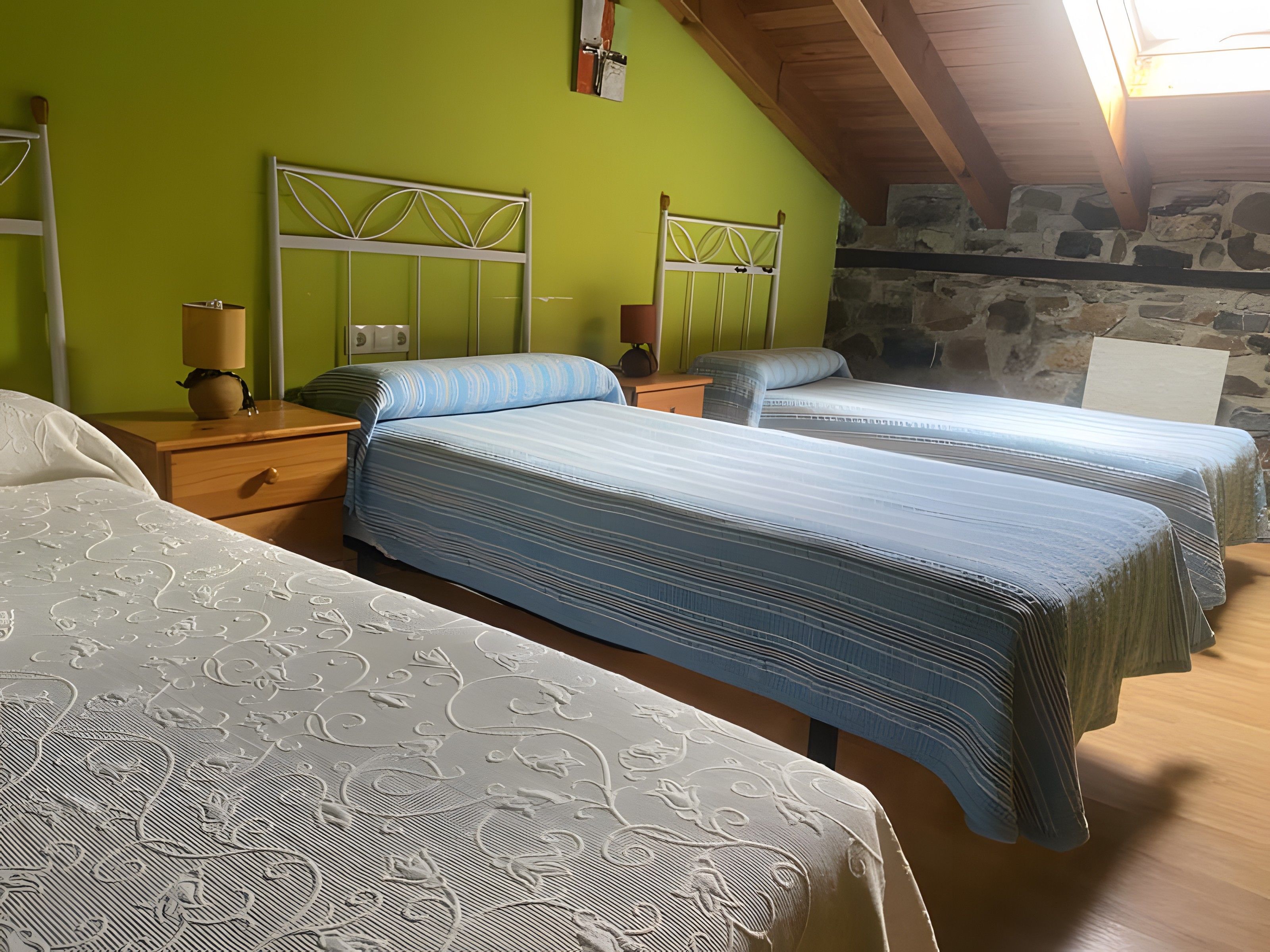 Una habitación con dos camas, una mesita de noche con una lámpara y una pared de piedra.