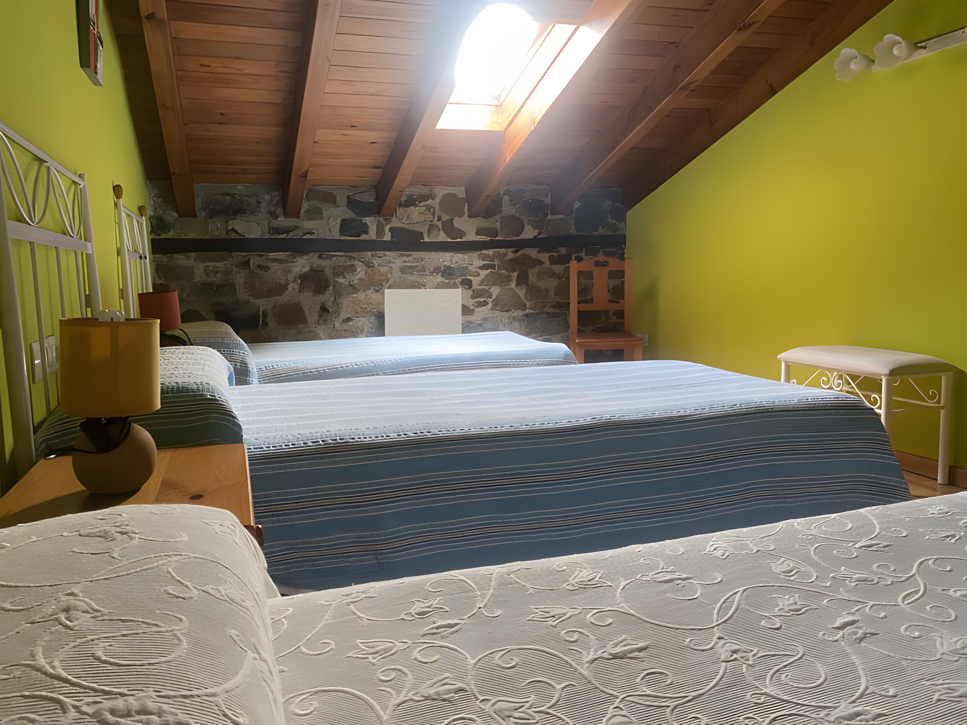 A room with two beds, a stone wall, a wooden ceiling, and a skylight.