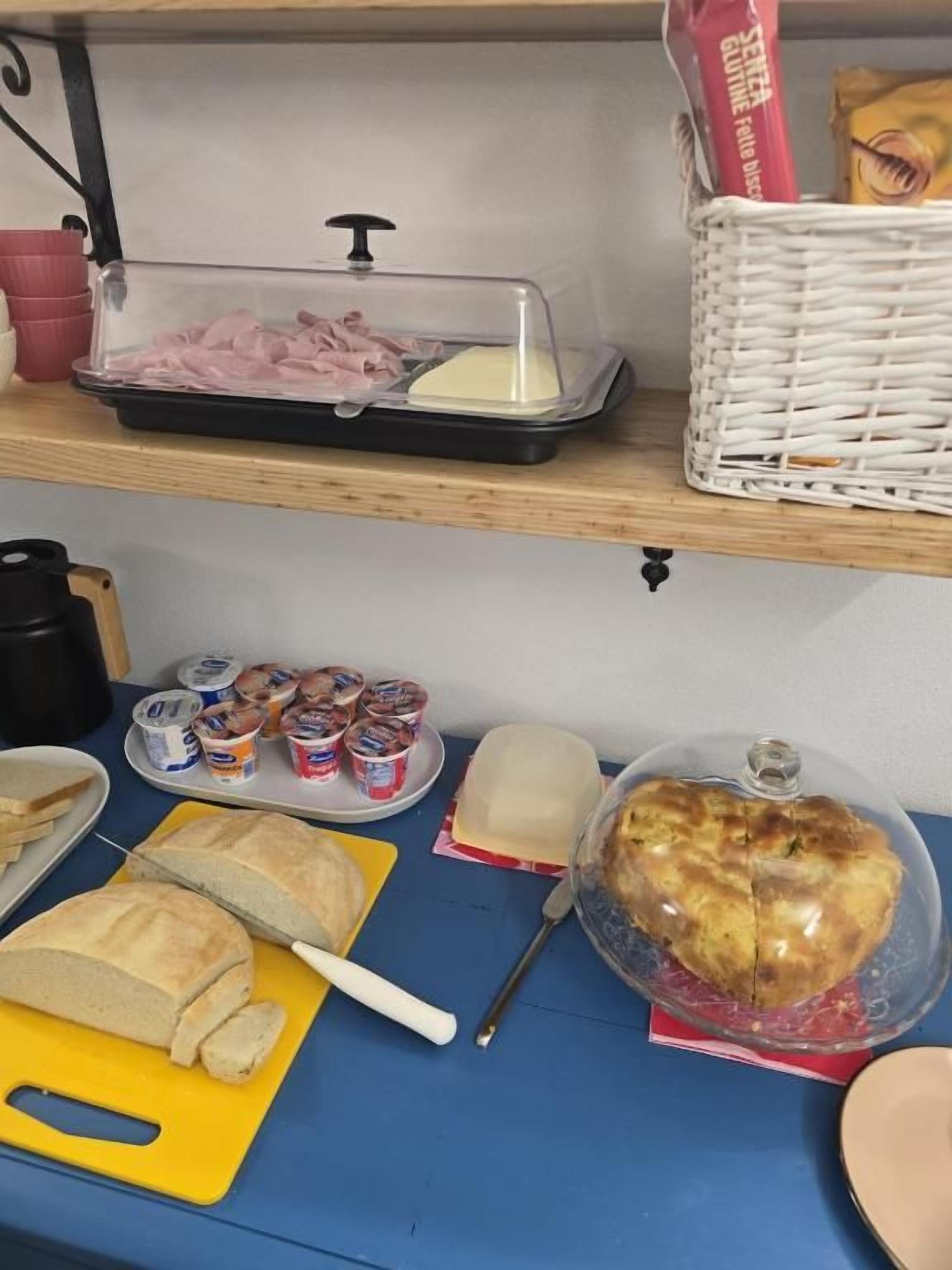 A buffet table with various food items including a covered ham tray, bread, butter, and a large covered pastry.