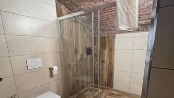 Un baño con cabina de ducha, inodoro y suelo de baldosas.