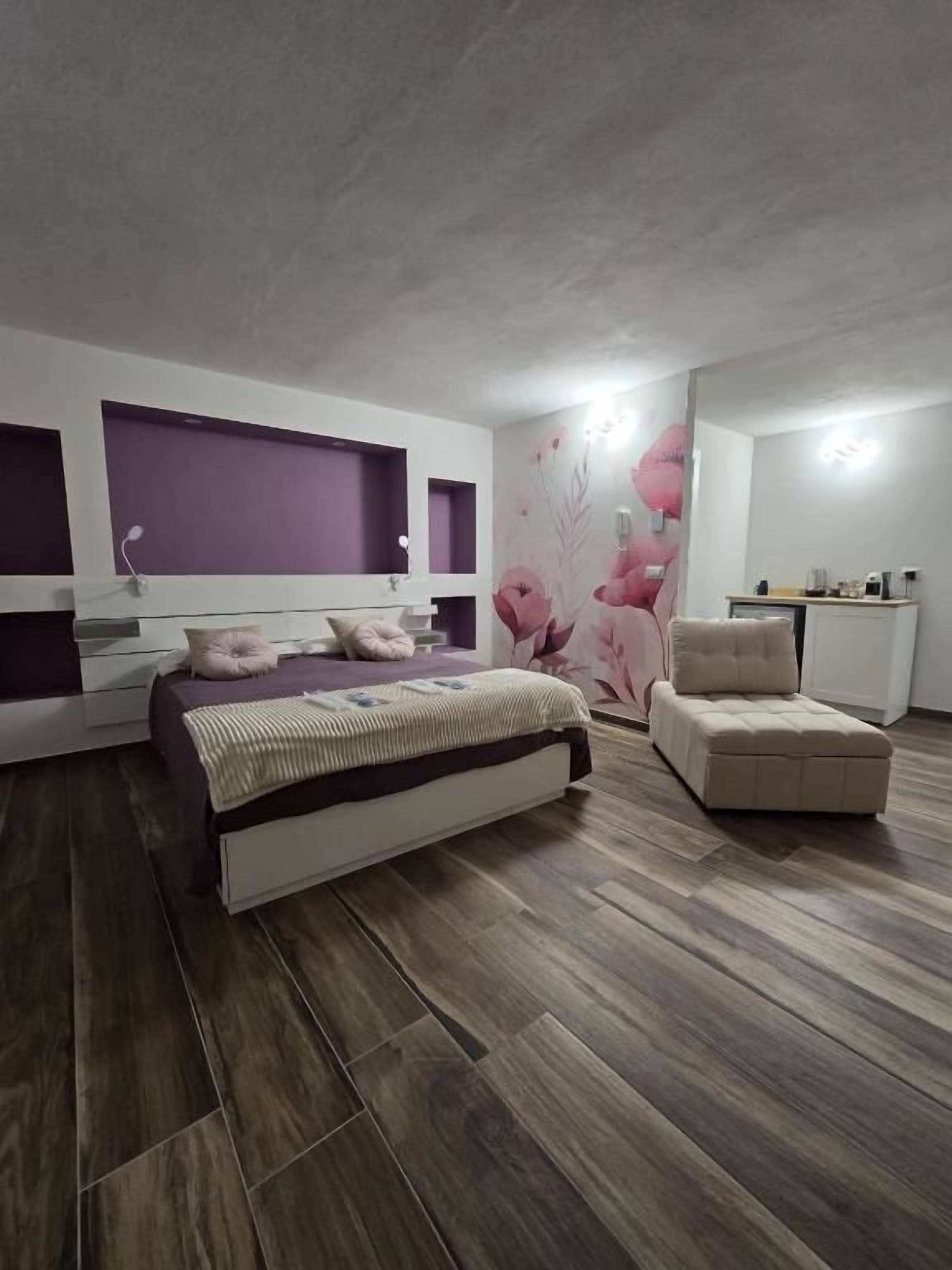 Un dormitorio con una cama, una silla, un aparador y una pared con papel tapiz floral.
