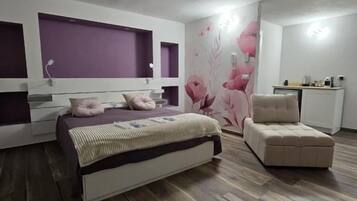 Un dormitorio con una cama, una silla, un aparador y una pared con papel tapiz floral.