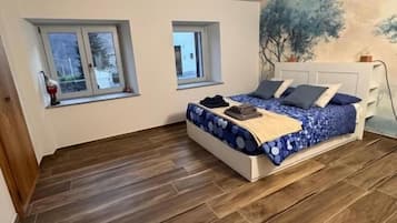 Makuuhuone, jossa on sänky, kaksi ikkunaa ja kalanruotokuviollinen lattia.