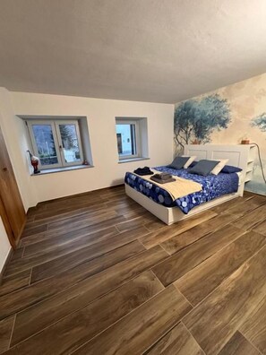 Een slaapkamer met een bed, twee ramen en een visgraatvloer.