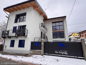 A two-story building with a balcony, a large window, and a gate with a logo. - B&B Blue Dragonfly (Paesana)