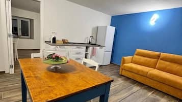 Una habitació amb taula de dinar de fusta, un sofà i una cuineta de fons.