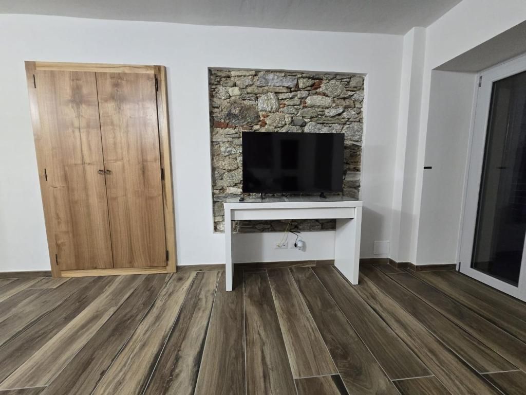 A room with a wooden wardrobe, a stone wall with a flat-screen TV, and a white console table.