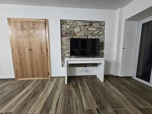 A room with a wooden wardrobe, a stone wall with a flat-screen TV, and a white console table.