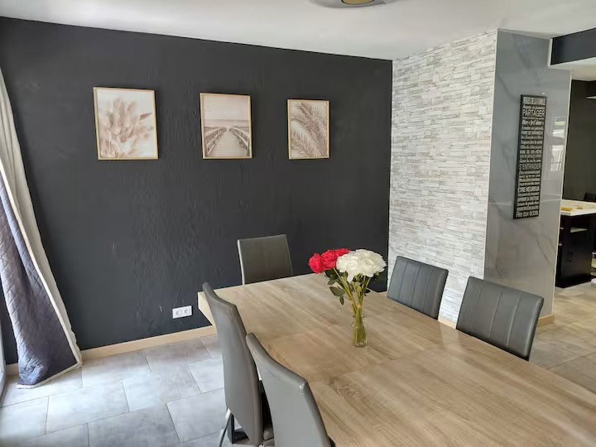 En spiseplads med et langt bord, grå stole og en vase med blomster.