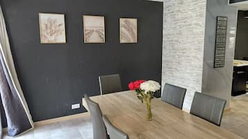 Un espace repas avec une longue table, des chaises grises et un vase rempli de fleurs.