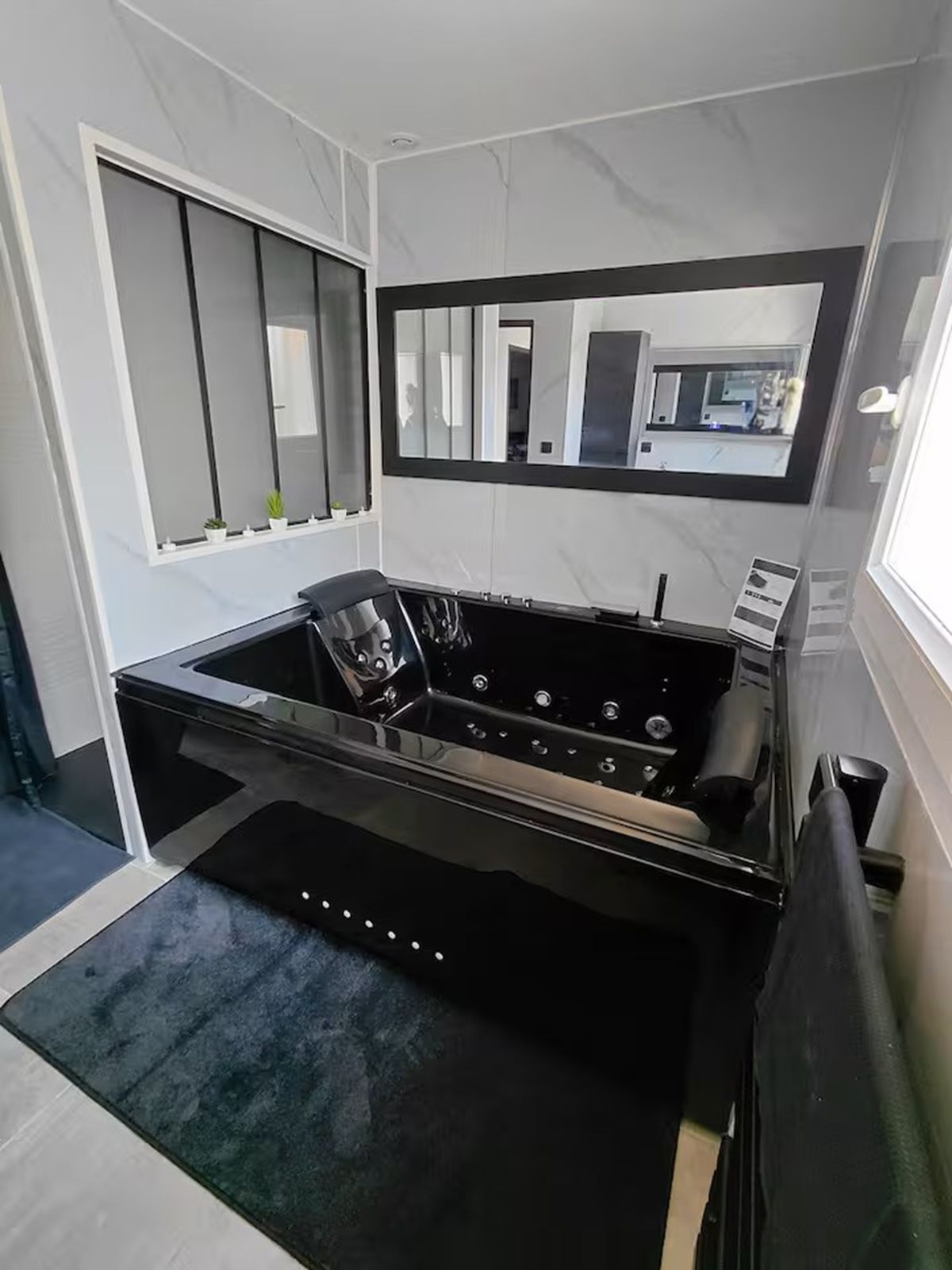 A modern bathroom with a black bathtub, a large mirror, and a small window.