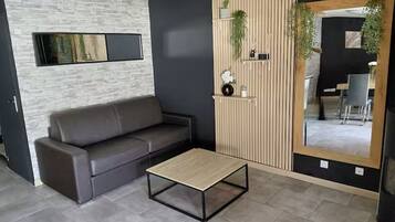 Un moderno salón con un sofá gris, una mesa de centro de madera y un espejo grande que refleja una zona de comedor.