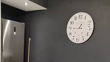 Eine moderne Küche mit einem Tisch aus Marmor, schwarzen Stühlen, einem Edelstahlkühlschrank und einer großen Wanduhr.