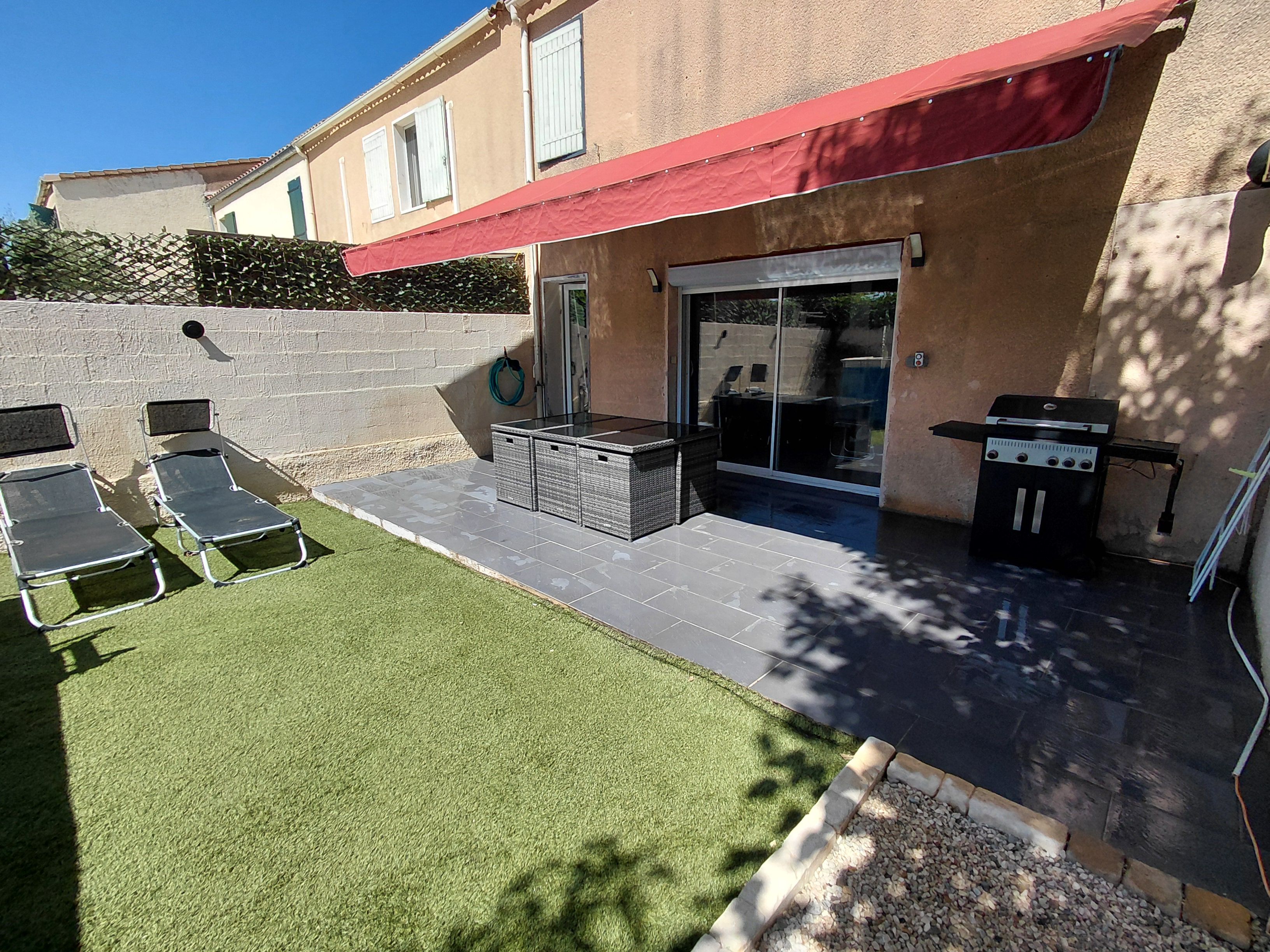 Eine Terrasse mit Grill, Sitzgelegenheiten im Freien und einer Glasdoor, die in einen überdachten Bereich führt.