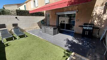 Eine Terrasse mit Grill, Sitzgelegenheiten im Freien und einer Glasdoor, die in einen überdachten Bereich führt.