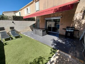 A patio with a barbecue grill, outdoor seating, and a glass door leading to a covered area.