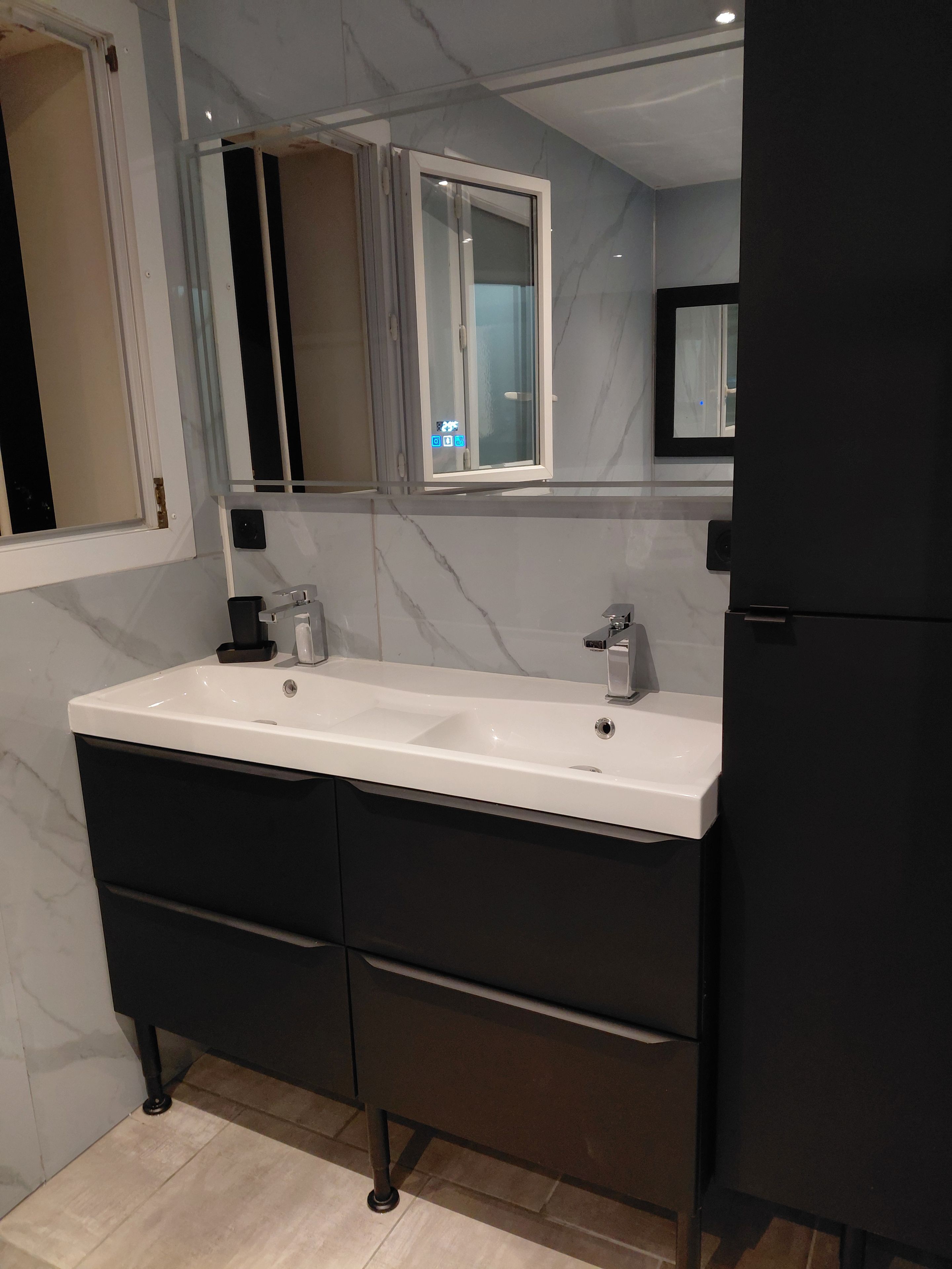 Un baño moderno con lavamanos doble, muebles de color oscuro y un espejo sobre el lavamanos.