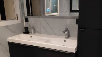 Un baño moderno con lavamanos doble, muebles de color oscuro y un espejo sobre el lavamanos.