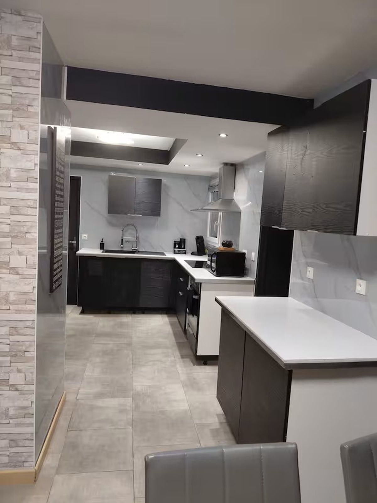Una cocina moderna con una isla central, muebles oscuros y encimera clara.