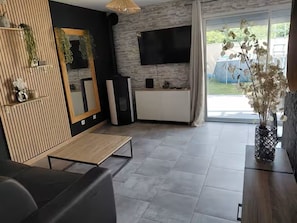 A modern living room with a flat-screen TV, a wooden accent wall, and a dining area.