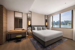A modern hotel room with a large bed, a desk, a chair, a nightstand, a mirror, and a view of a cityscape. - Fraser Suites Reserve Bangkok (Bangkok)
