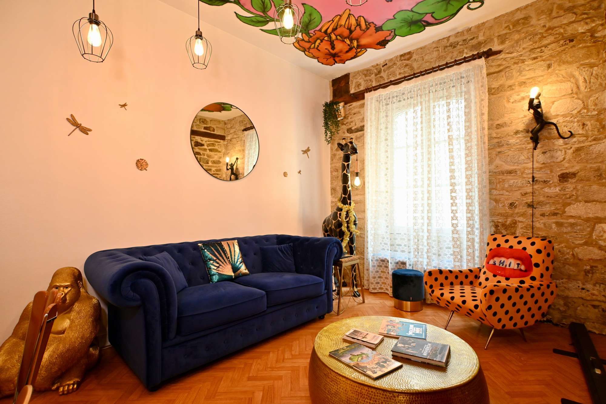 A living room with a blue sofa, a round coffee table with books, a giraffe statue, and a polka dot chair.