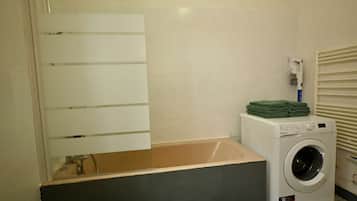 A laundry area with a washing machine, a drying rack, and a towel dispenser.