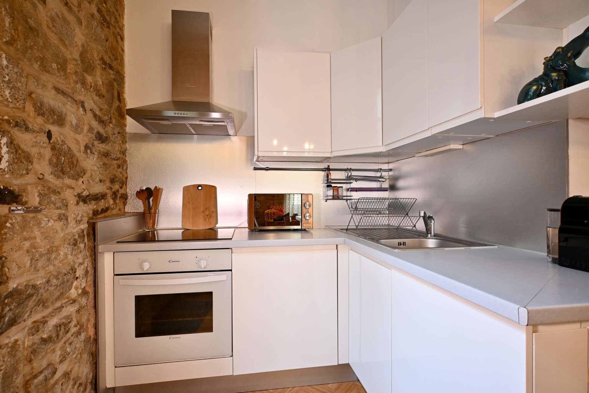 A modern kitchen with white cabinetry, a stainless steel range hood, and a built-in oven.