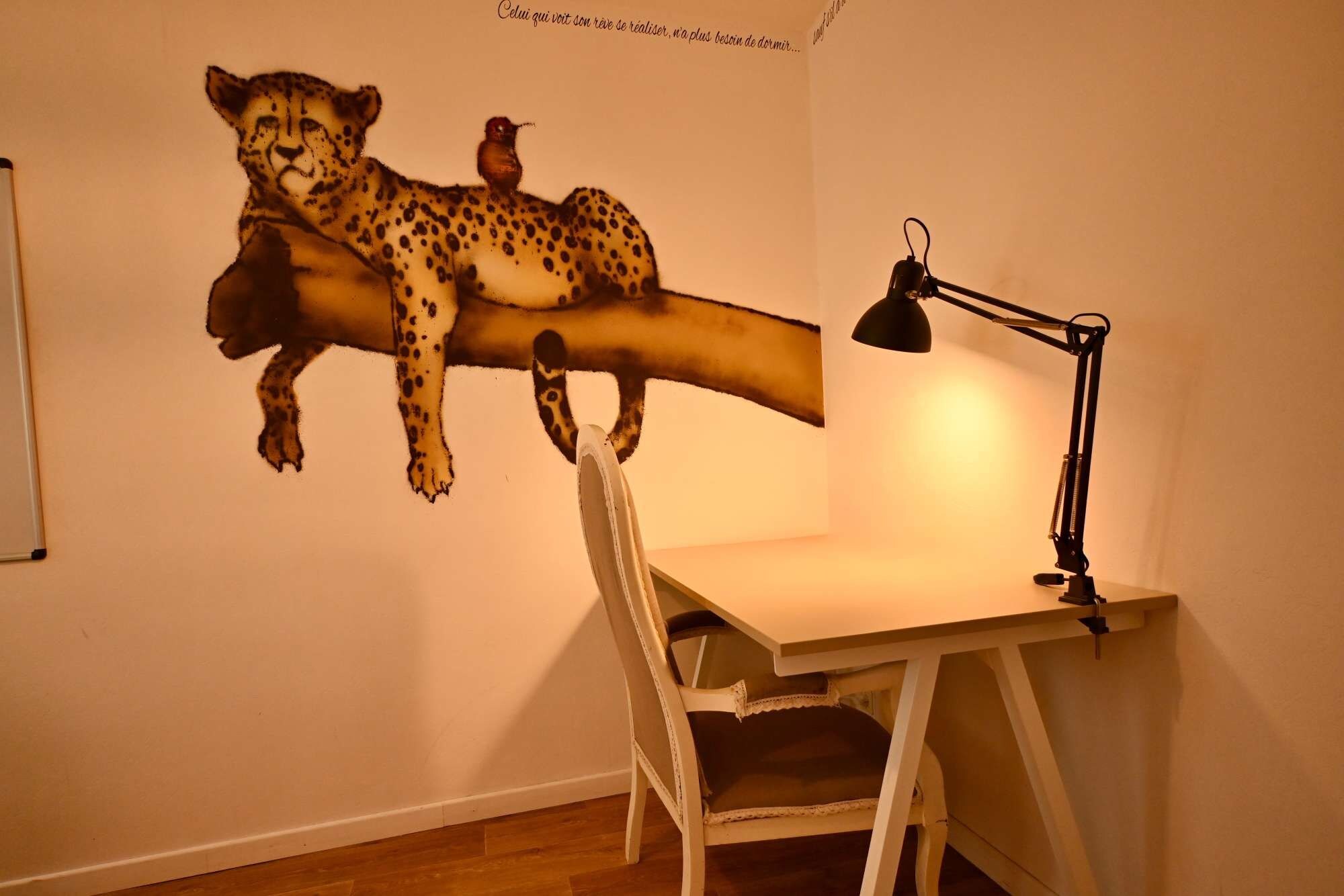 A room with a desk, chair, and a wall-mounted artwork of a cheetah and a bird.