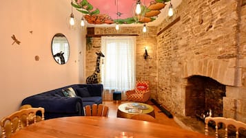 A cozy living room with a stone wall, a fireplace, a round wooden table, and a blue sofa.
