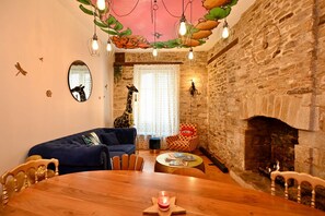 A cozy living room with a stone wall, a fireplace, a round wooden table, and a blue sofa. - Historic Center Apartment – Fireplace, Stone Walls & Jungle Decor (Vannes)